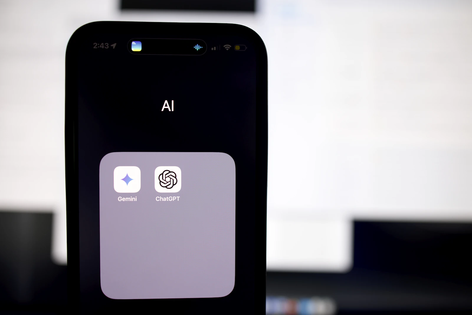 A smartphone showing an AI app folder with Gemini and ChatGPT — the AI assistants that now recommend businesses to Singapore buyers